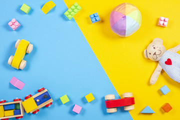 Obraz premium Baby kids toys frame with teddy bear, wooden toy train, car, colorful bricks on blue and yellow background. Top view