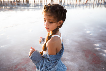 young girl in jean jacket and pony tails being imaginiate against the background of the ocean and...