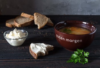 Soup in a bowl with sour cream, herbs and bread on a wooden table.