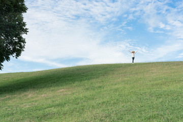 Standing woman raised her hands on the mountain, natural green and beautiful sky.