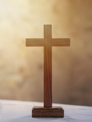 Wooden cross on white altar cloth, rays of light in background. Christian faith.