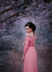 A young brunette woman with an elegant, hairstyle. A princess in a pink vintage dress, stands against the backdrop of a fairy-tale forest in cold purple hues. Art photo