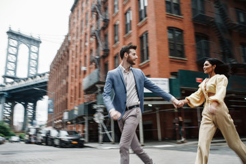Love story in New York. Indian woman in bright yellow clothes and handsome American man hold each other hands walking around the New York - obrazy, fototapety, plakaty