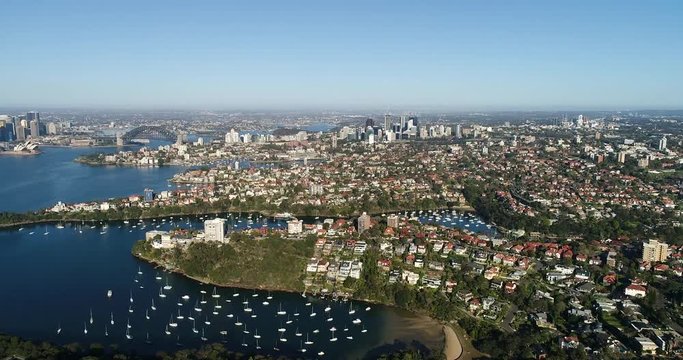 Side to side wide aerial rotation over Sydney harbour waterfront from Mosman suburb on North Shore in view of distant city CBD landmarks and the Harbour Bridge.
