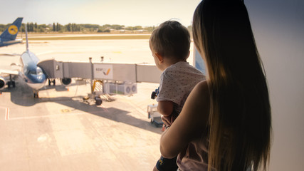 Toned image of little boy with mother looking through big window in airport terminal