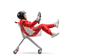 Elderly man in a racing suit with helmet holding a steering wheel and sitting inside a shopping cart