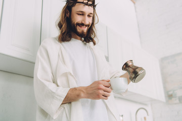 low angle view of happy Jesus pouring coffee from cezve into cup in kitchen during morning time at home