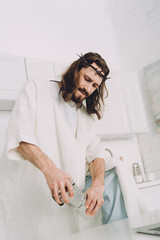 low angle view of Jesus grinding coffee beans with hands in manual coffeemill in kitchen at home