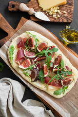 Flatbread pizza with ham, figs, arugula on wooden board. Top view