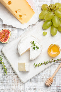 Brie or camembert cheese served with fruits and honey on white cheeseboard. Top view