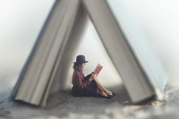 kleine frau, die ein buch liest, das durch ein haus aus einem riesigen buch geschützt ist © Cristina Conti