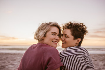 Smiling young lesbian couple watching a beach sunset together