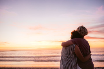 Affectionate lesbian couple watching the sunset by the ocean