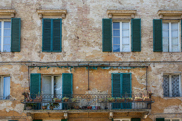 Green shuttered windows and balcony on a weathered building in Siena, Tuscany, Italy
