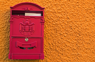 A bright red post box with two white envelopes on bright yellow orange wall. Loket, Czech Republic