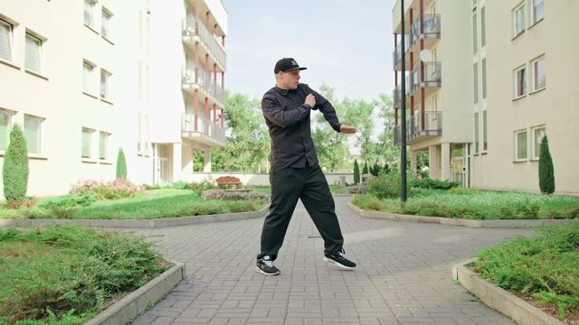 A young man dressed in black breakdancing in the street. Long shot