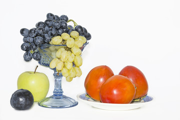 red persimmon on a blue plate, apple, grapes