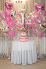 cake from several tiers for the first birthday on a background of decor of balloons with the inscription in Russian Marusya 1 year old