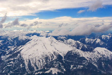 Blick auf gewaltige schneebedeckte Berge umgeben von dramatischen Wolken vor blauem Himmel.