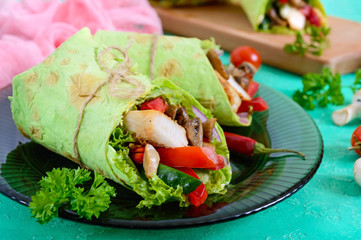Burrito with chicken, vegetables, mushrooms in pita bread with spinach on a wooden table. Mexican food.