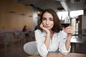 Young woman holding red wine glass sitting in the restaurant leaning head to hand