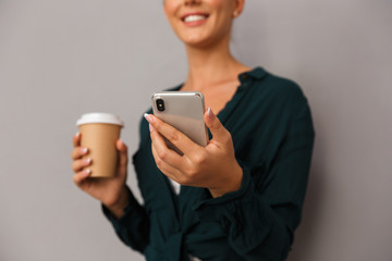 Beautiful business woman posing isolated over grey wall background drinking coffee talking by mobile phone.