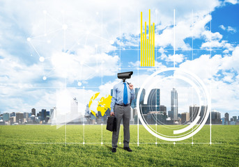 Camera headed man standing on green grass against modern cityscape