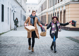 Cheerful teenager couple with paper bags walking down the street in winter.