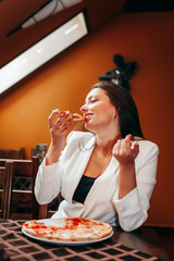 Beautiful stylish brunette girl in white jacket eating pizza at restaurant.