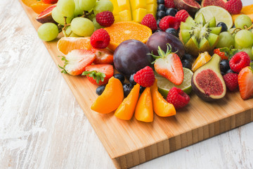 Healthy raw fruits and berries platter, strawberries raspberries oranges plums apples kiwis grapes blueberries, mango on the serving board, top view, copy space, selective focus