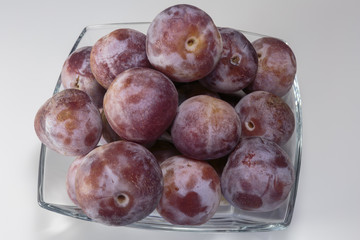 Ripe fresh plums in a glass dish over the white background. Vegan food.