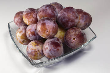 Ripe fresh plums in a glass dish over the white background. Vegan food.