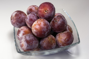 Ripe fresh plums in a glass dish over the white background. Vegan food.