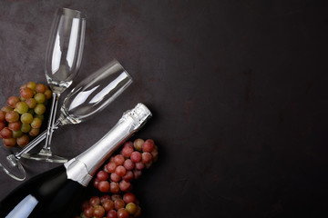 Wineglasses, grapes and bottle of champagne lying on black wooden background. New Year celebration concept. Top view. Flat lay.