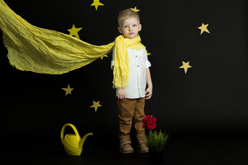 a little boy in a yellow scarf against the night sky with stars near a red rose and yellow watering...