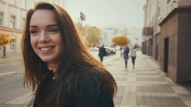 Smiling model in casual clothes walking in slow motion at autumn city. Close up face of attractive woman. Beautiful girl walking at daylight in street
