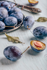 Plums with leaves and knife over wooden surface