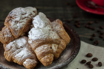 Cup of cappuccino coffee and croissant on dark table