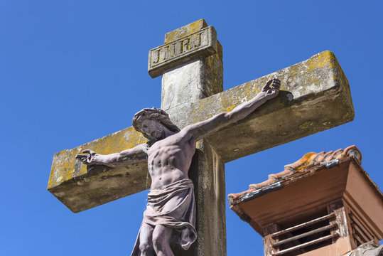Jesus on the cross from below with red roof and blue sky in the background - concept religion Christianity Jesus Christ god symbol faith mourning sacrifice prayer savior heaven power