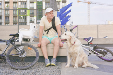 modern life in a big city - sporty young man with dog resting on a bench in the city after a bike ride