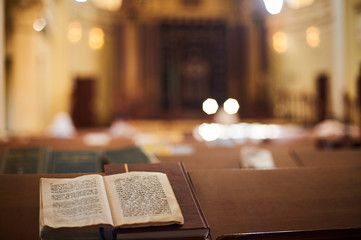 Inside of Orthodox Synagogue with open book in the Hebrew language in the foreground. selective focus - obrazy, fototapety, plakaty