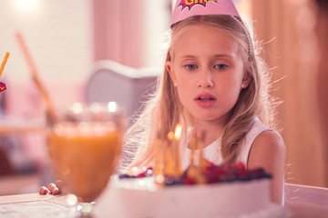 Thoughtful kid. Calm birthday girl thoughtfully looking at the cake and making a wish