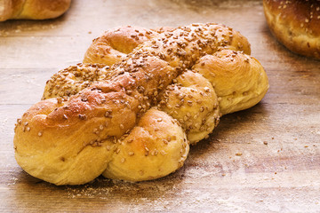 Close-up of bread braid with sesame seeds on wooden background.