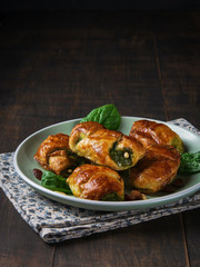 Mini spinach croissants with raisins, pinions and goat cheese and with a bowl of spinach on the plate with dark background. Space for text, vertical. Healthy concept. Close-up.