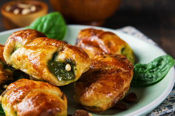 Spinach croissants with raisins, pinions and goat cheese and with a bowl of spinach on the plate with dark background. Space for text, horizontal. Healthy concept. Close-up.