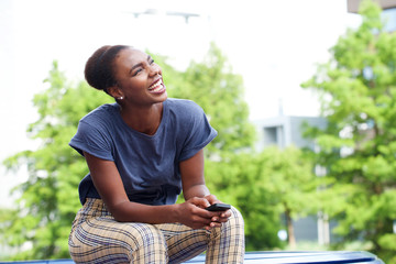 beautiful young african american woman laughing with mobile phone outdoors