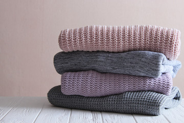 A pile of warm sweaters on a wooden table on a light background. Autumn and winter clothes.