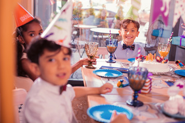 Kids with juice. Positive relaxed kids enjoying birthday party and sitting at the table with glasses of juice