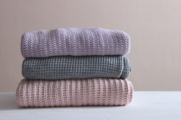 A pile of warm sweaters on a wooden table on a light background. Autumn and winter clothes.