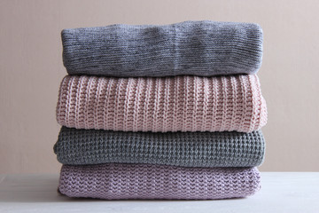 A pile of warm sweaters on a wooden table on a light background. Autumn and winter clothes.